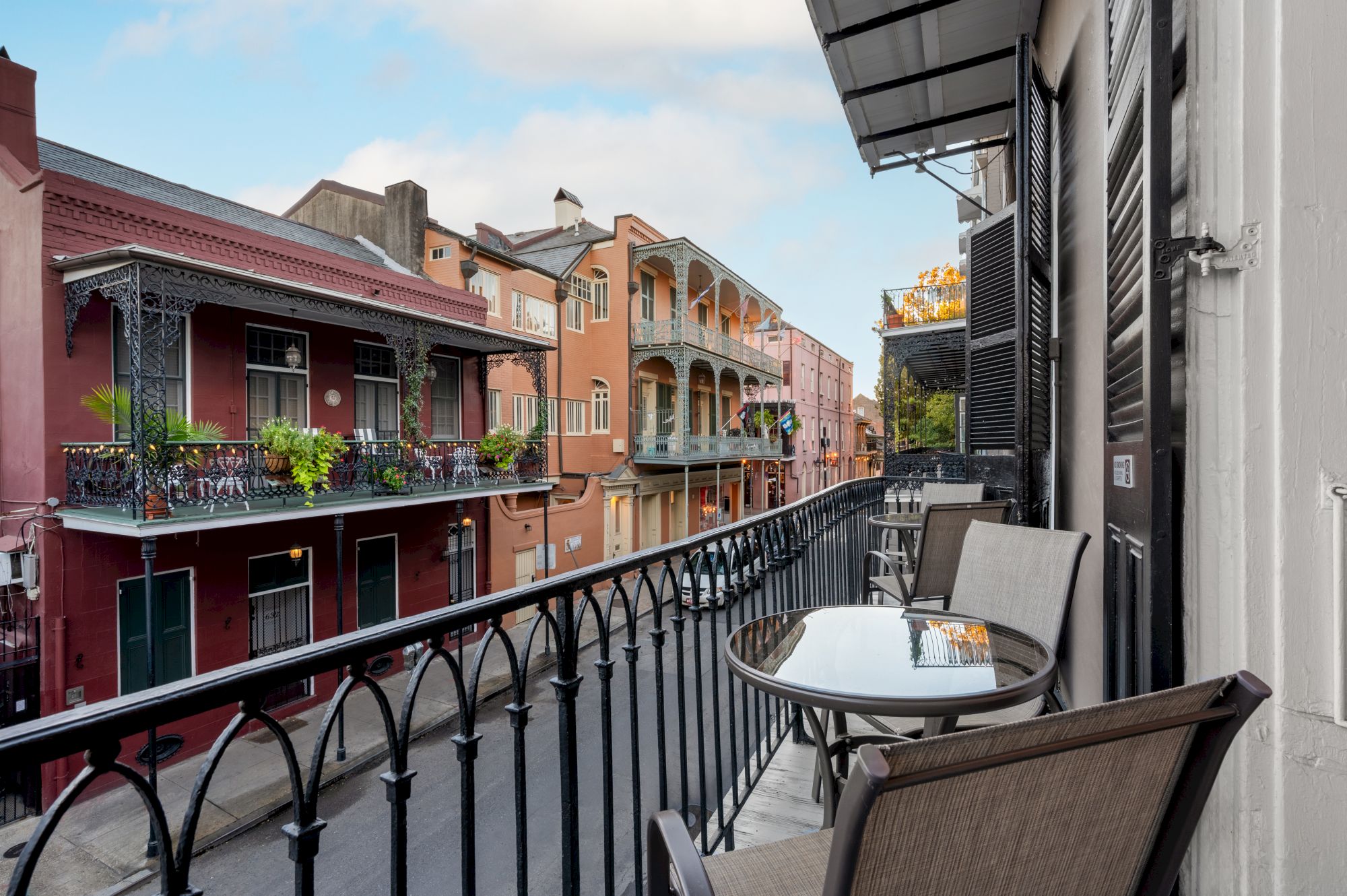 A balcony overlooking a colorful street with ornate buildings and railings, featuring outdoor seating and some greenery around.