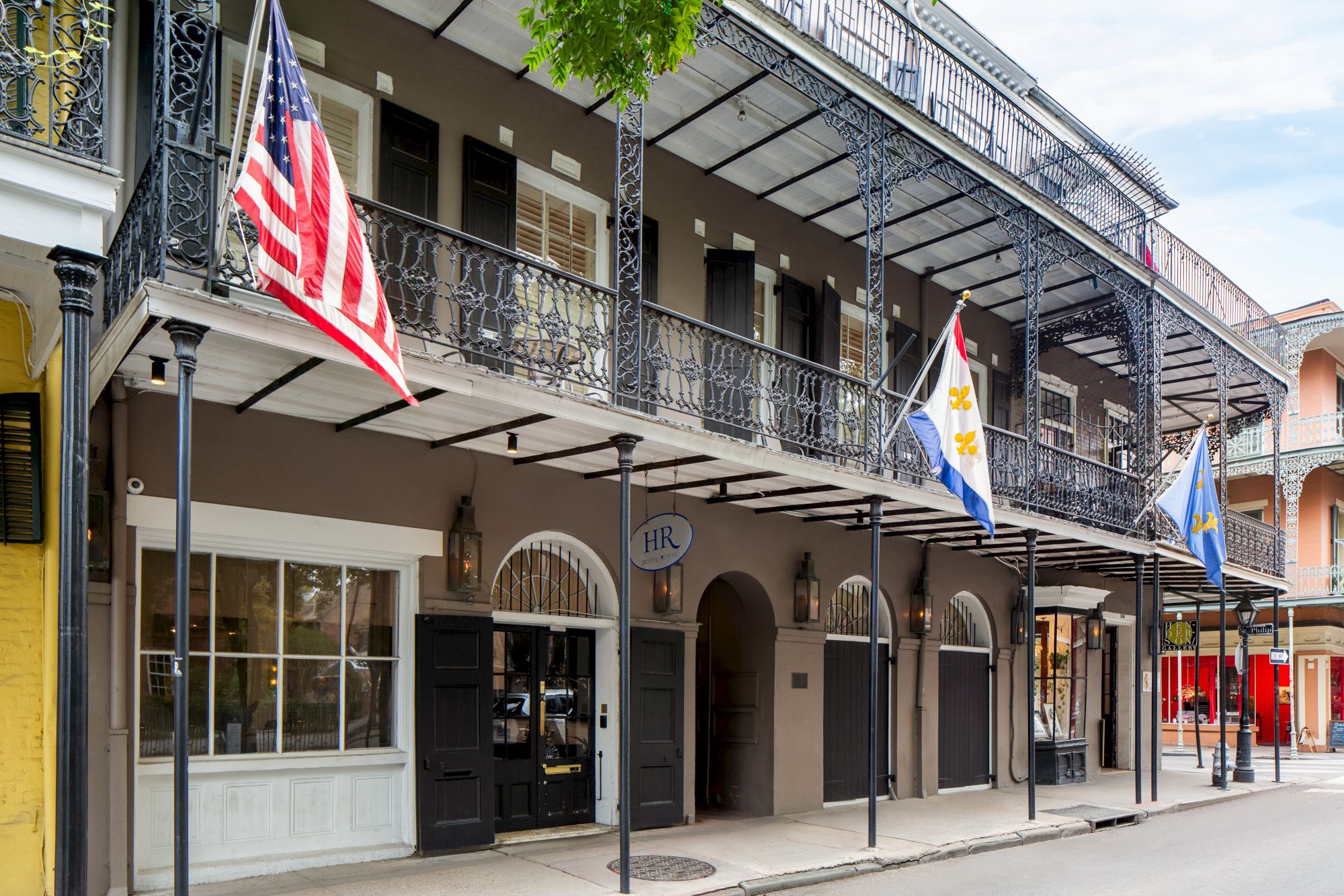 A building with wrought iron balconies, displaying American and two other flags, located on a quiet street.