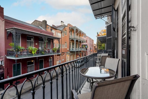 A balcony with a table and chairs overlooks a street with colorful buildings and decorative wrought iron railings.