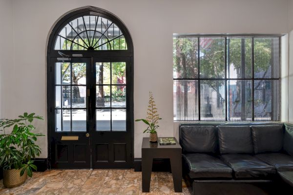 A cozy room with a black door, large window, plants, a black couch, and a small table, with natural light coming in.