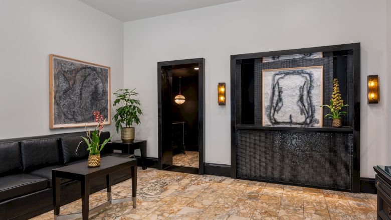 A modern room with abstract art, seating with a table, plants, and stone flooring. The design is minimalistic with a calming vibe.