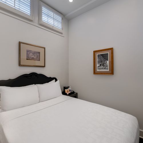 A cozy bedroom with a neatly made bed, rustic lamp on the side table, two framed pictures on the walls, and a flat-screen TV.