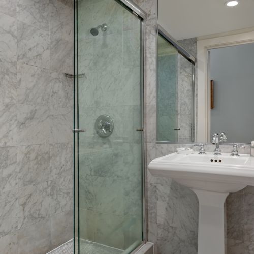 A modern bathroom with marble walls, glass shower, pedestal sink, and toilet. Minimalist design and clean aesthetic throughout.